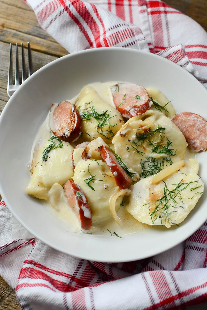 A white bowl with pierogies sitting on a red and white cloth napkin.