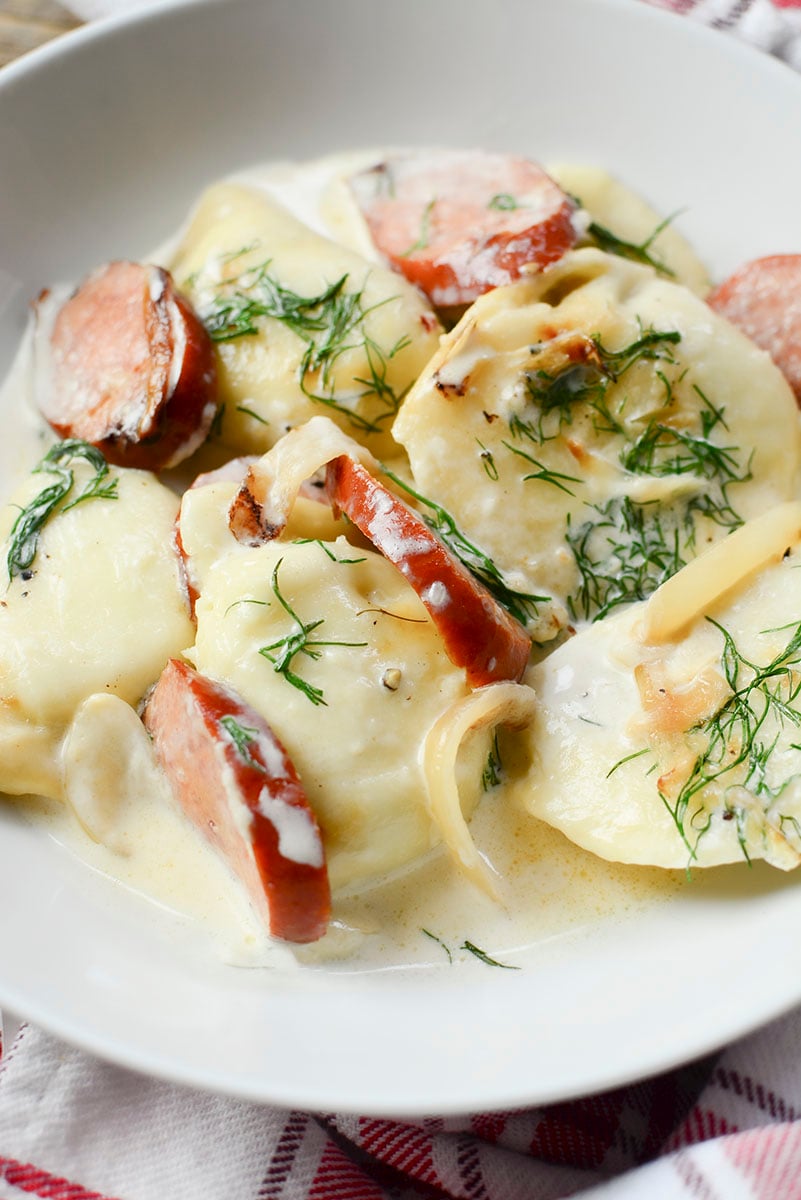 5 pierogies with sausage and dill in a white bowl. 