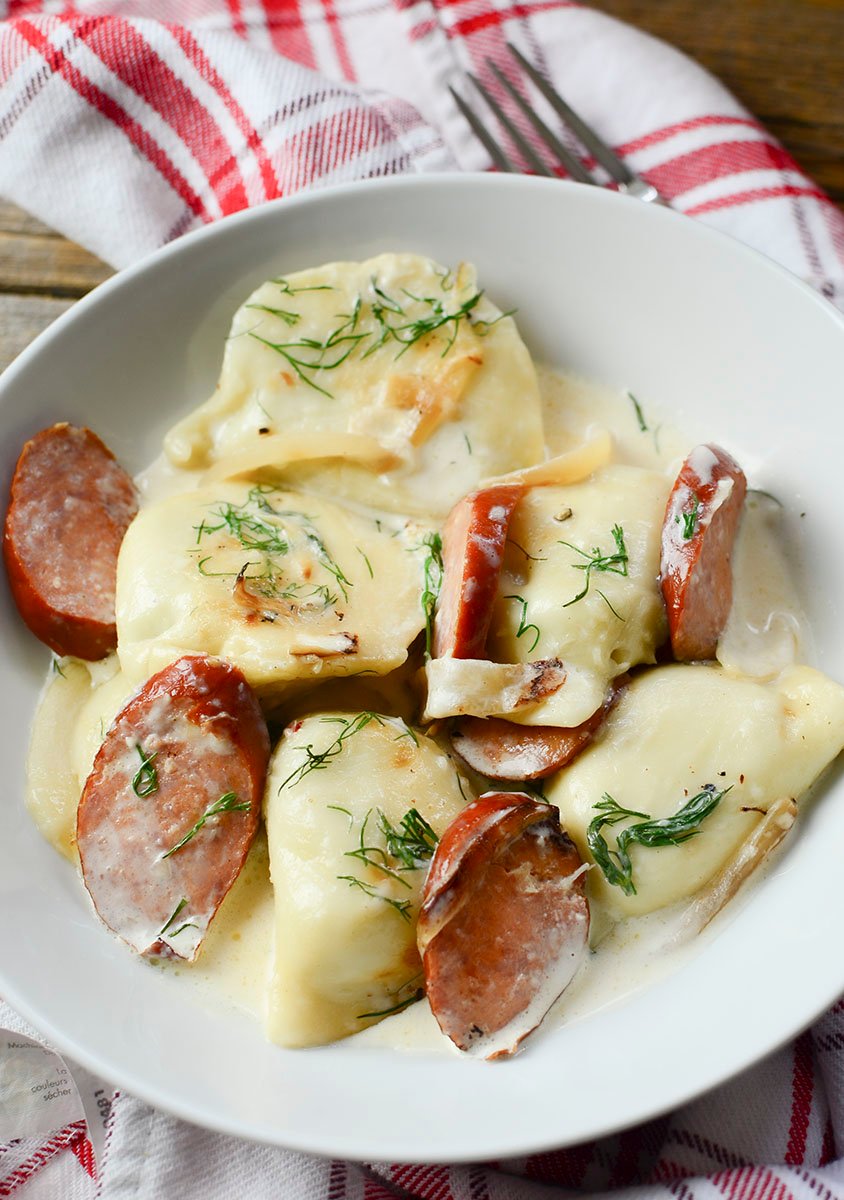 Pierogies and dill sauce in a white bowl.