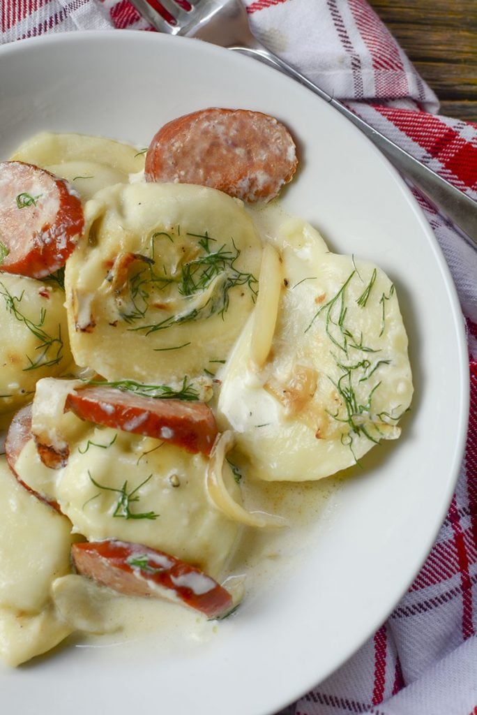A half plate photo of perogies with onions, sausage and dill. 