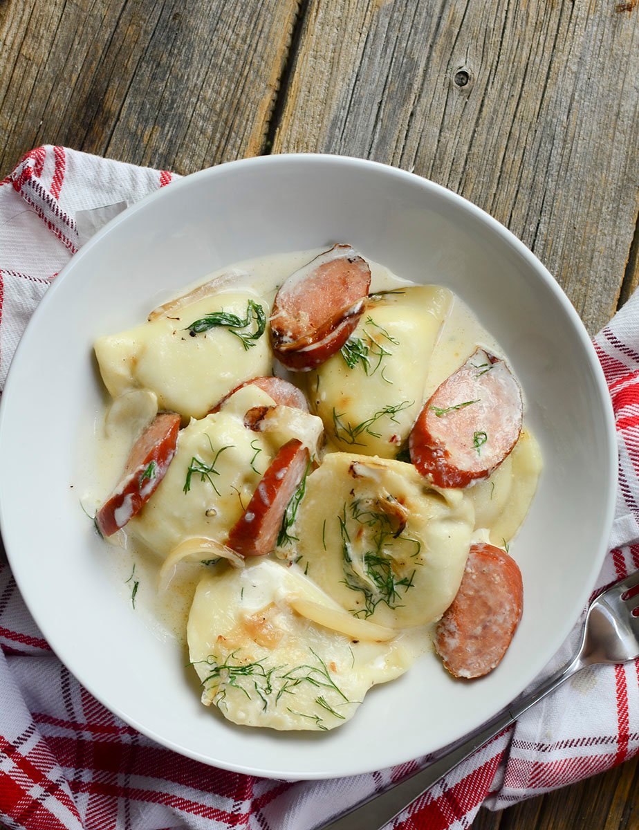 Perogies and cream sauce with sausage on a wooden background.