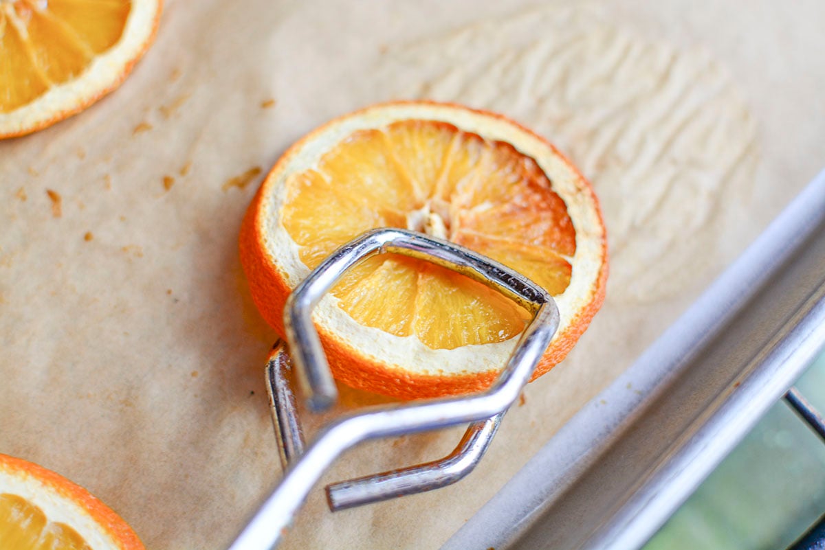 A peice of dried orange is being flipped over to dry the other side, using a metal flipper. 