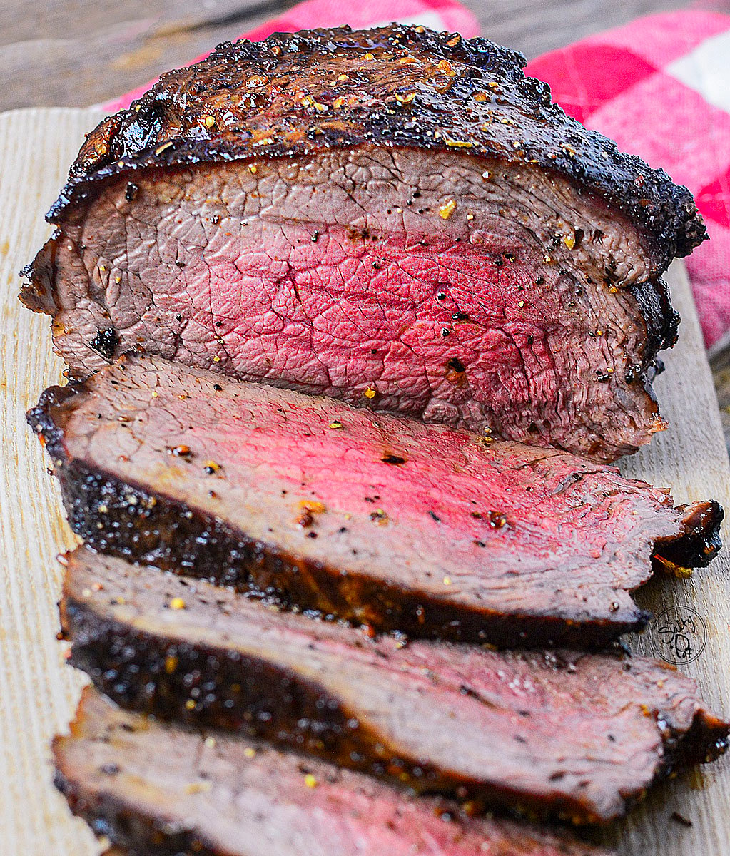 An air fried beef roast, sliced, on a cutting board. The beef is cooked to medium rare doneness.