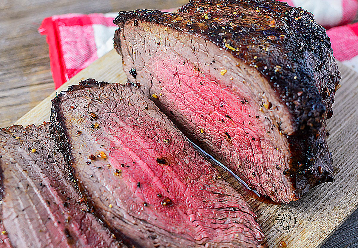 Air fryer roast beef, cut into slices, on a wooden cutting board.