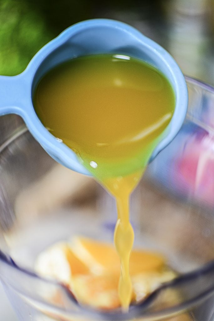 Mango juice being poured into the blender from blue tupperware measuring cups!