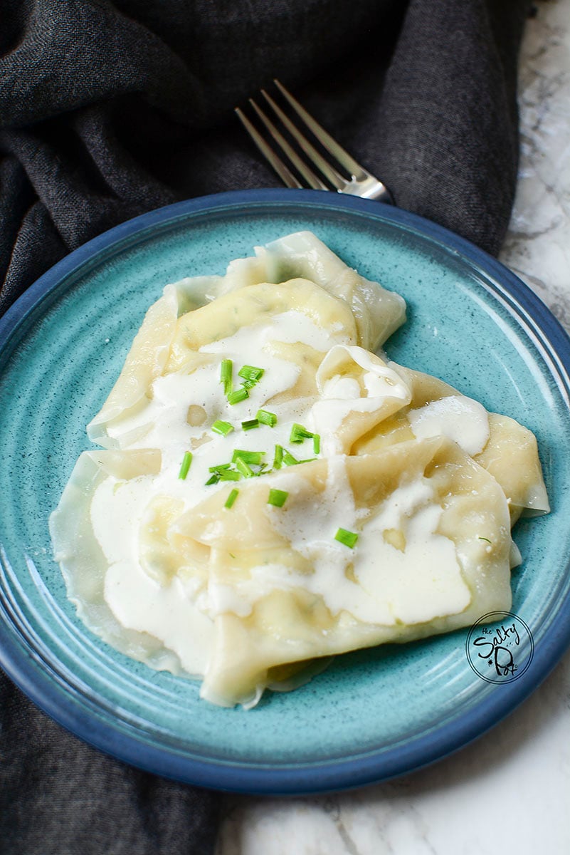 Four cheese filled dumplings with cream drizzled over top and some chopped chives. 