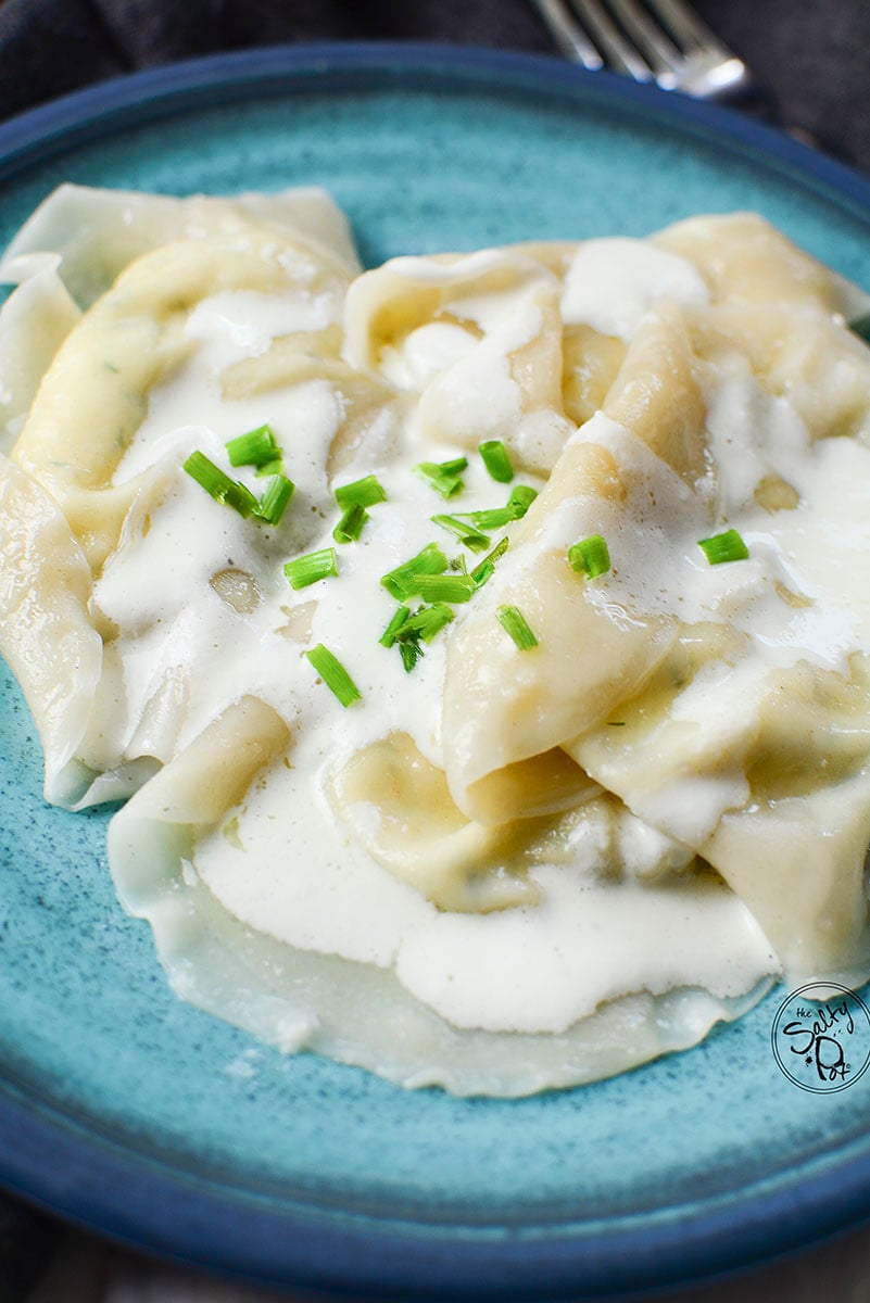 A close up of the dumplings with cream on a blue plate.