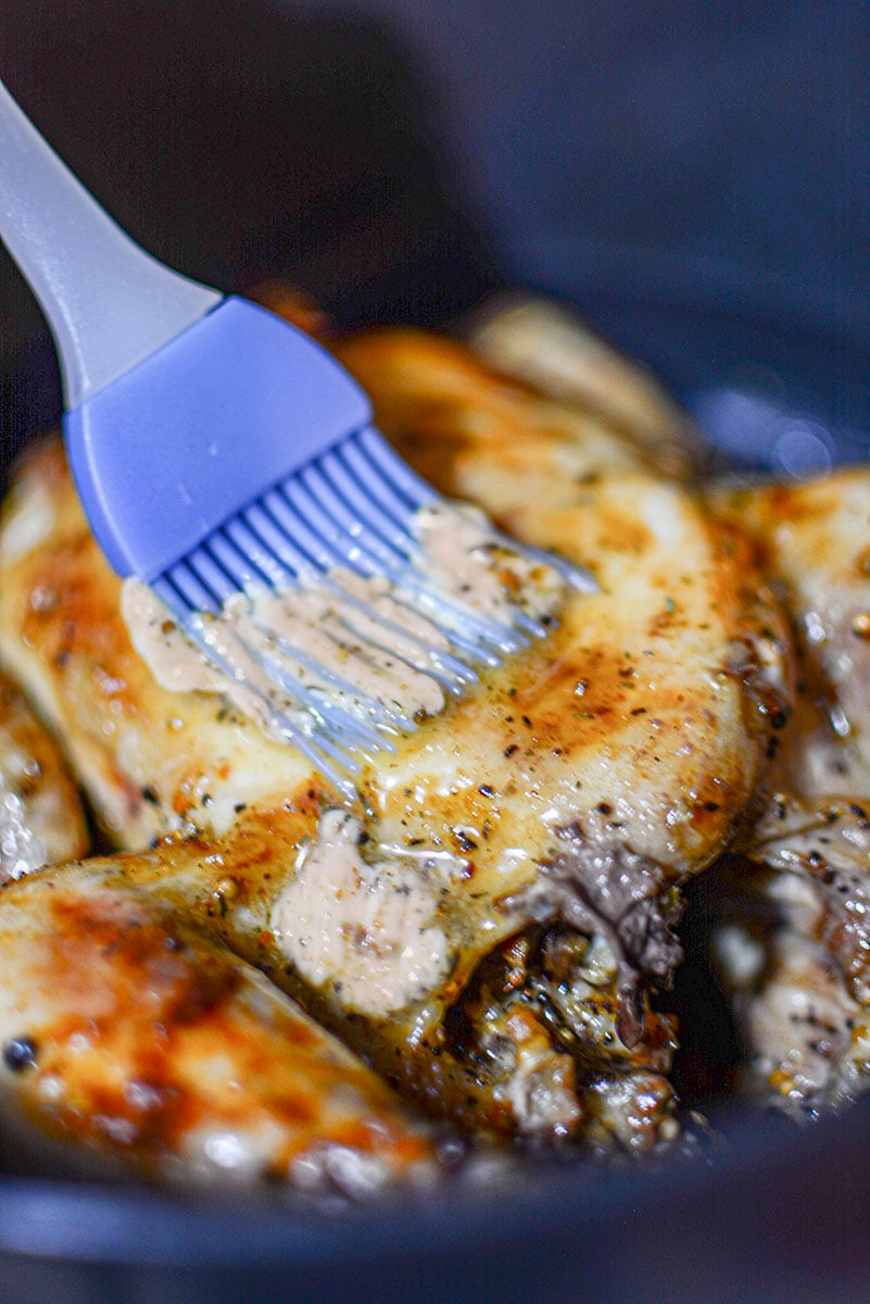 A blue silicon brush basting the bird with seasoned butter.