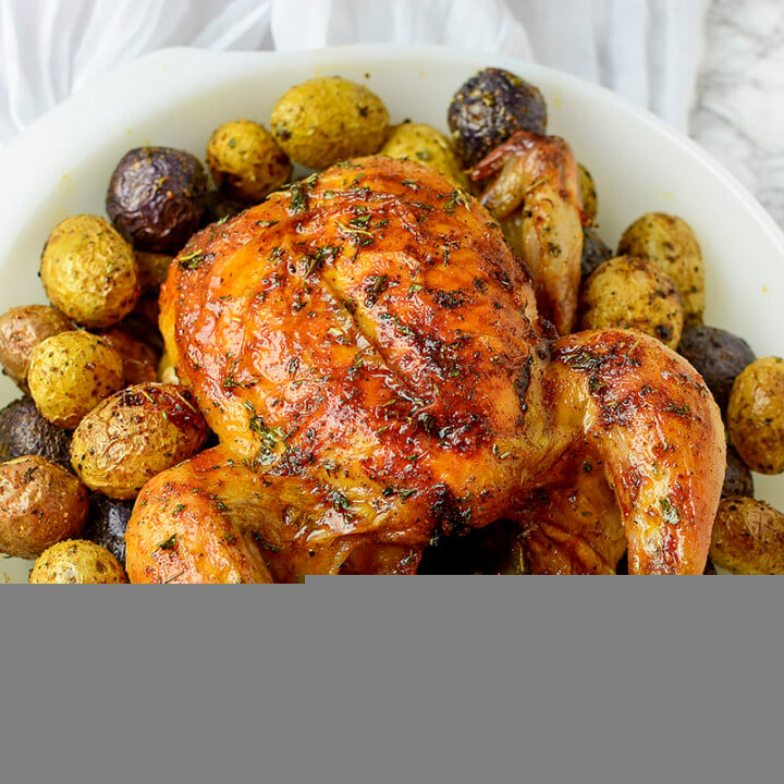 An air fryer cornish hen surrounded by potatoes in a white dish.