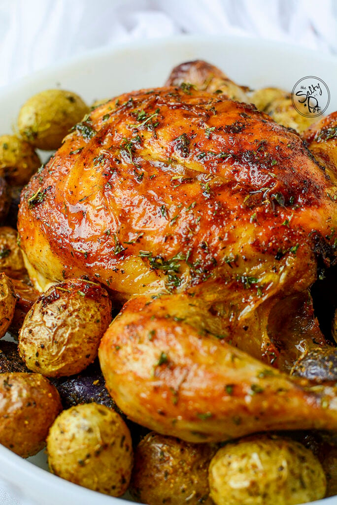 A cooked cornish hen in a baking dish with seasoned potatoes surrounding it.