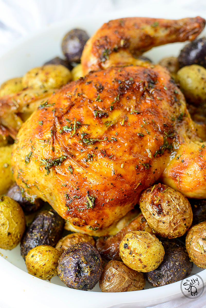 A breast side up game hen sitting on a bed of potatoes after being air fried.