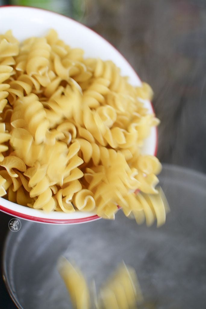 Pouring dry rotini pasta into boiling hot salted water to cook. 