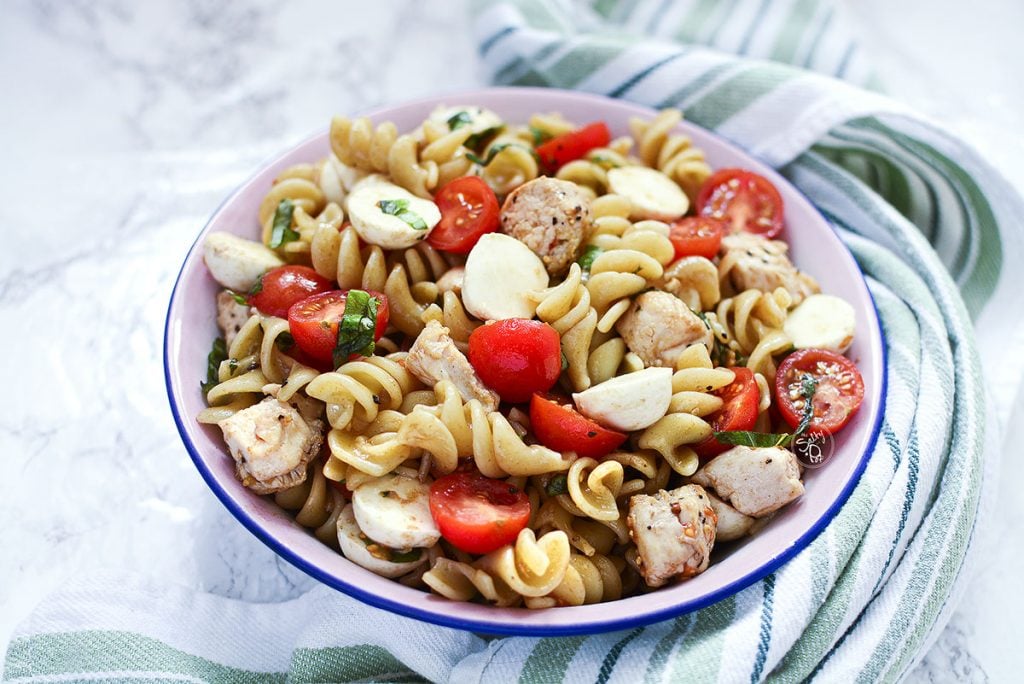 A 45 degree angle of the pasta salad with a green and white striped towel around the bowl. 