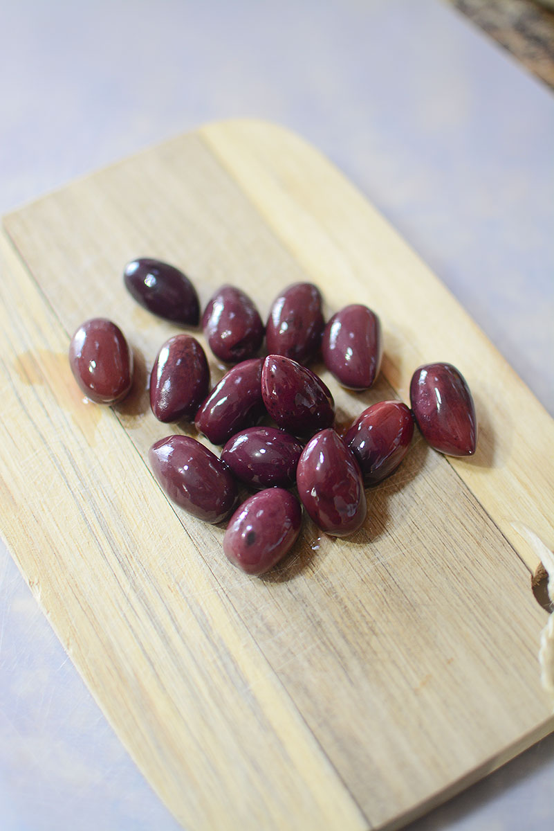 Black olives on a wooden cutting board.