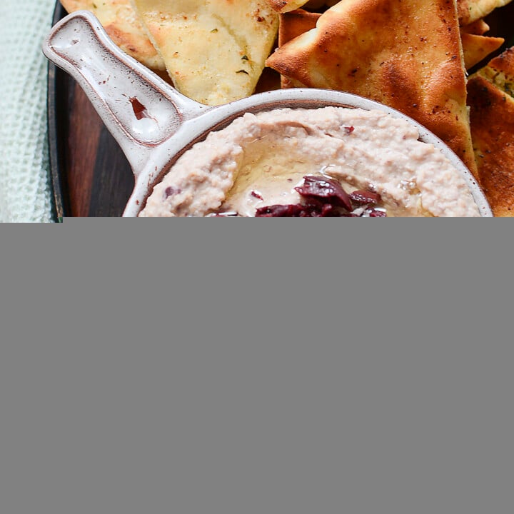 Black olive hummus in a dish with pita chips beside it.