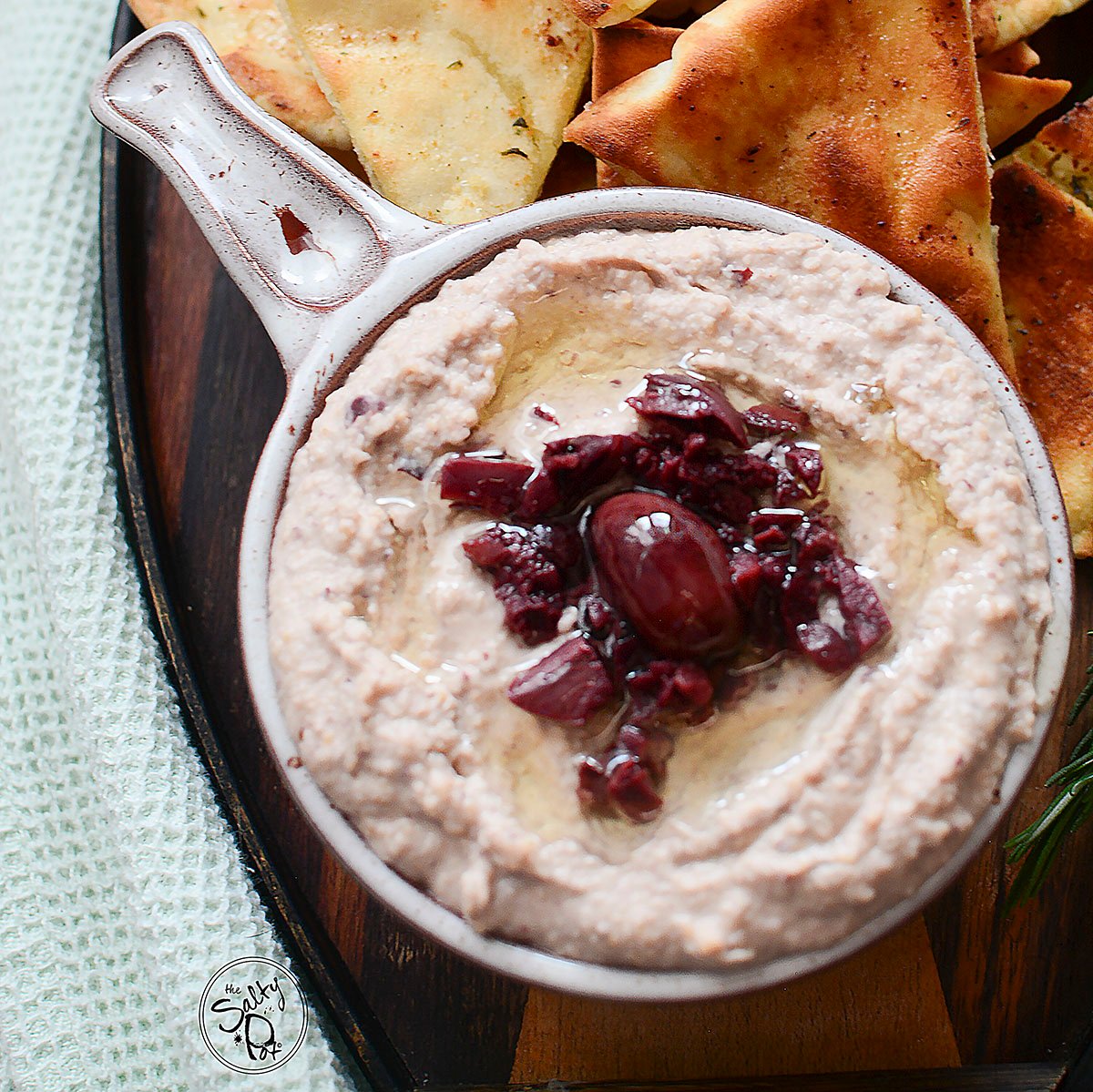 An overhead image of the hummus recipe. Minced black olives in the center of the dip with drizzled oil over the surface, ready to eat!