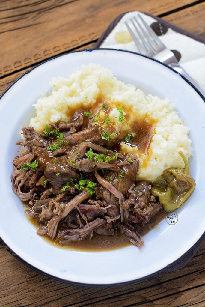 The Mississippi Beef Roast sitting on a white plate with gravy and mashed potatoes.