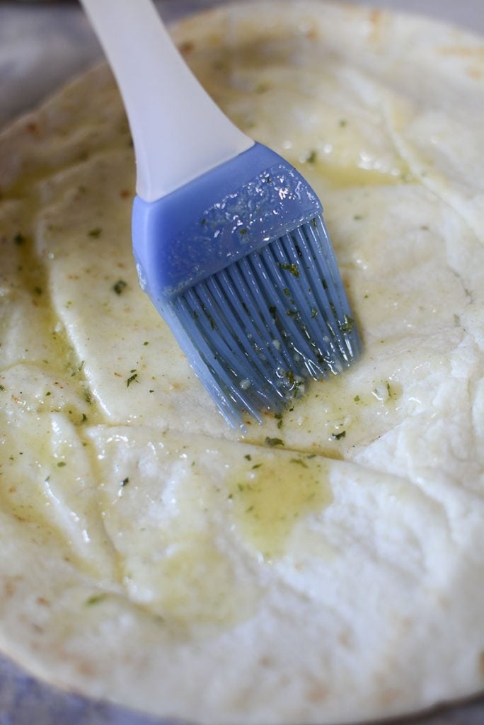 Brushing garlic butter onto the surface of the pita with a blue basting brush.