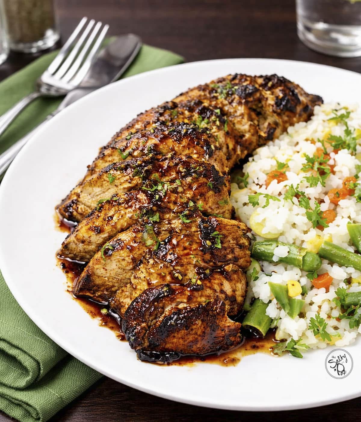 Balsamic chicken on a white plate with a green napkin beside it.