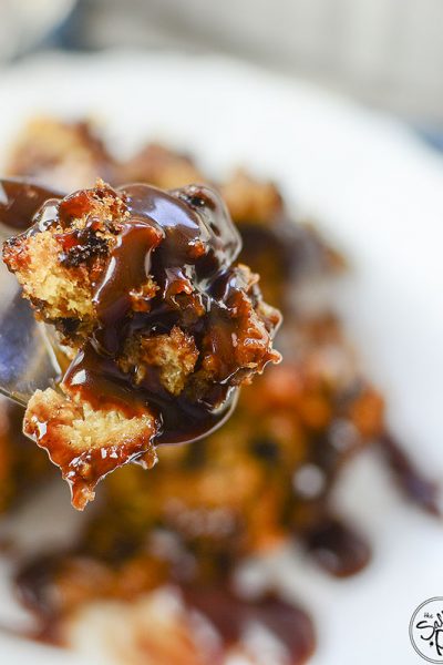 A bite of chocolate pecan bread pudding with drizzled chocolate sauce on a spoon.