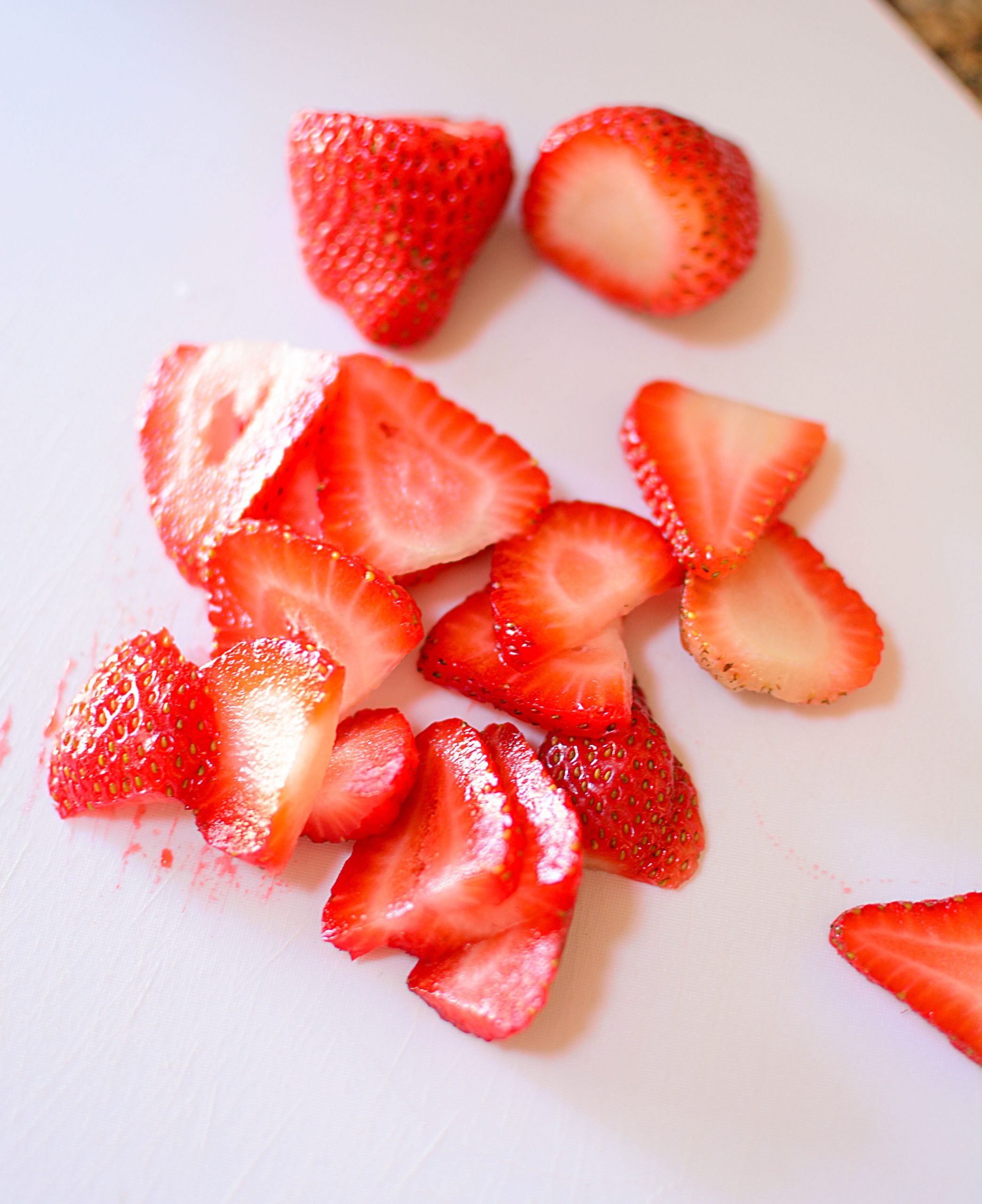 Sliced strawberries on a white plastic cutting board.