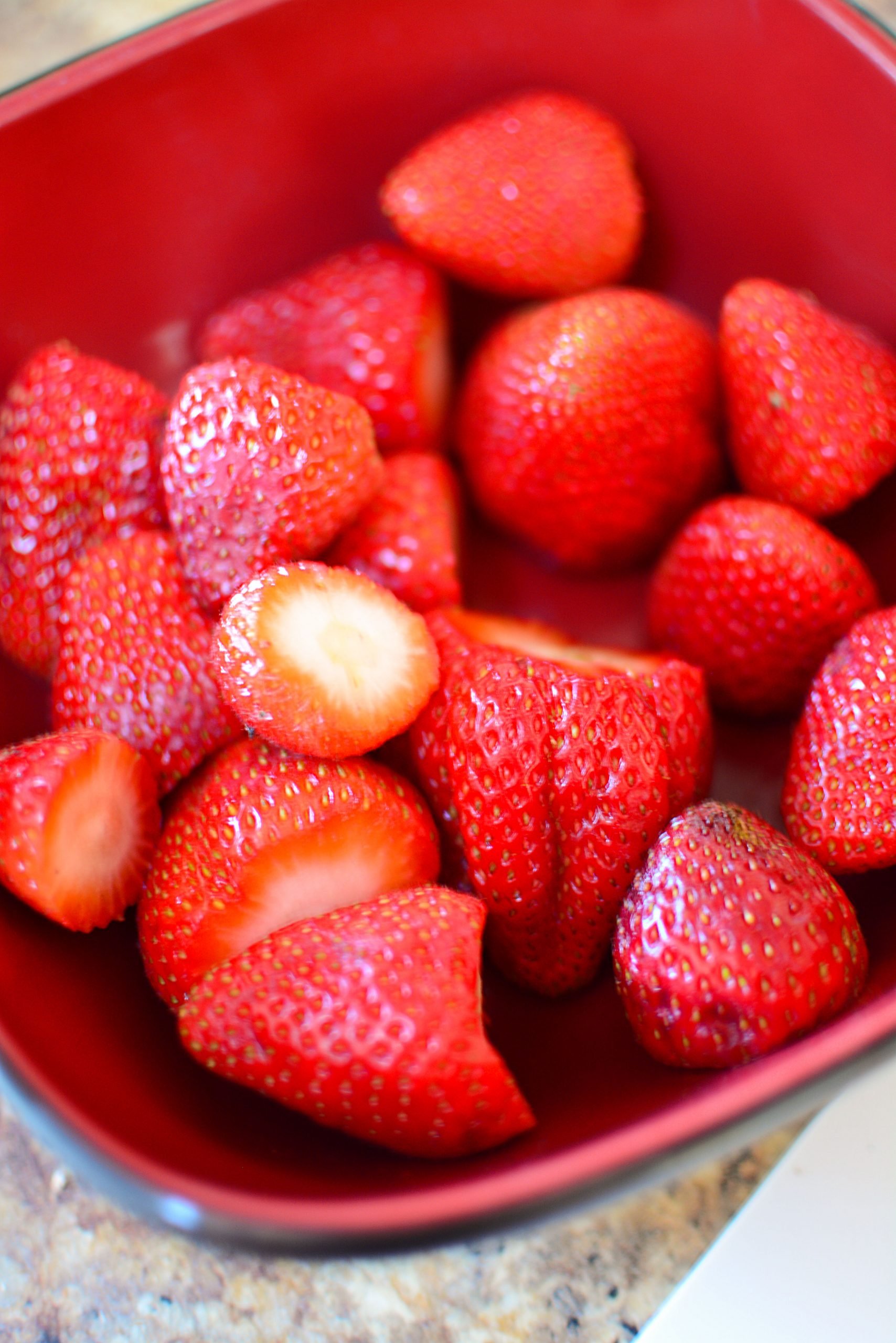 Fresh strawberries in a red bowl.