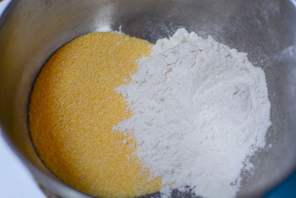 Cornmeal and flour in the bottom of a silver mixing bowl.