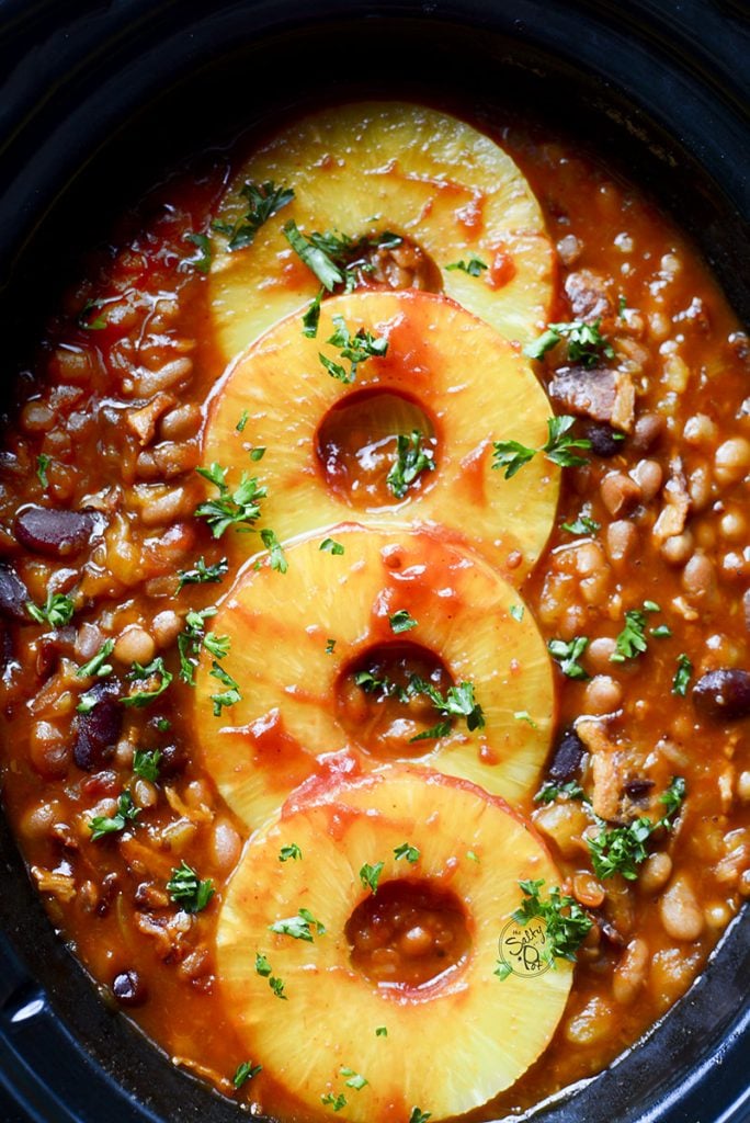 The baked beans in a slow cooker bowl with rings of pineapple going down the center.