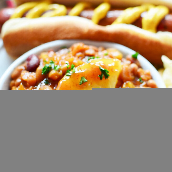 A bowl of baked beans with sausage in the background