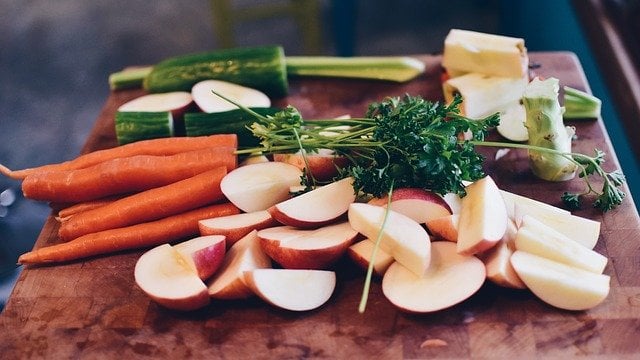 A photo of carrots, apples, cucumbers and parsley on a cutting board.