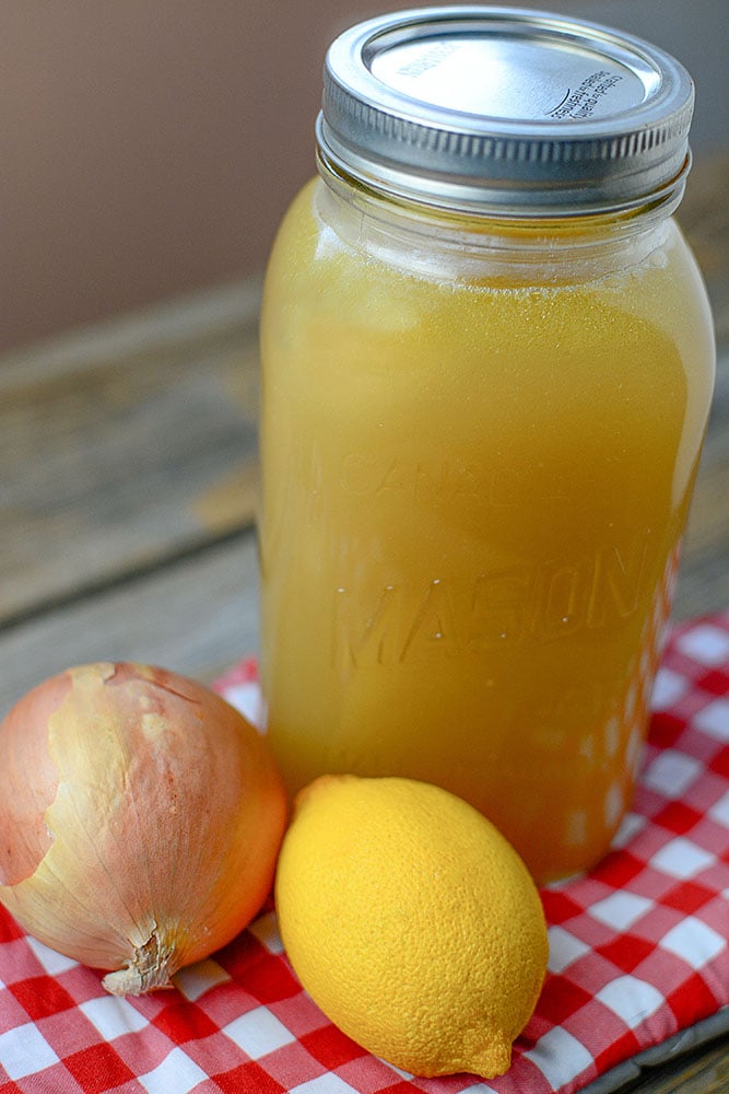 A mason jar full of chicken bone broth with an onion and lemon sitting in front of it.