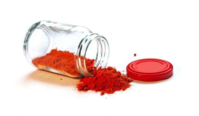 A jar of spice (maybe paprika) dumped on it's side with some of the spice falling out from it.