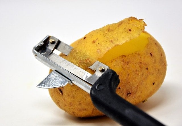 A potato peeler taking off the skin of the potato.