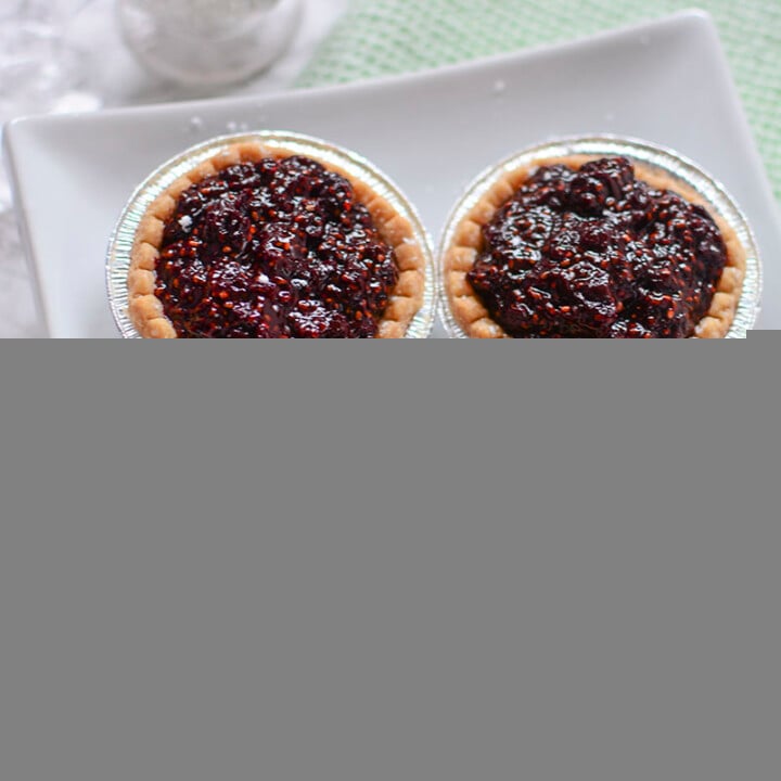 Three cherry tarts are sitting on a white plate with a shaker of icing sugar in the background.