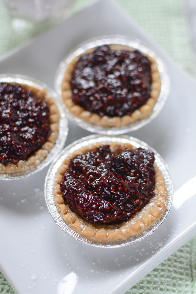 Three pretty sour cherry tarts sitting on a white square plate.