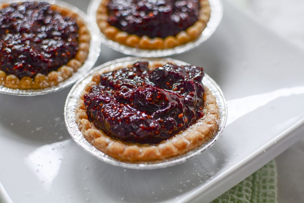 A closeup, 45 degree angle of the tarts on a white plate. The cherry filling is mounded in the center of the tart and looks delicious!