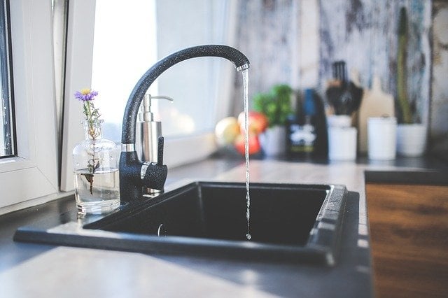 A kitchen sink from the side view with water running into the sink. 