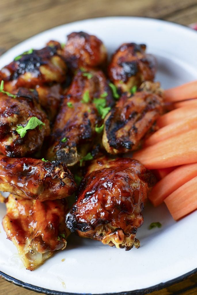 A closeup of a few sauced chicken wings sitting on a white tin plate.