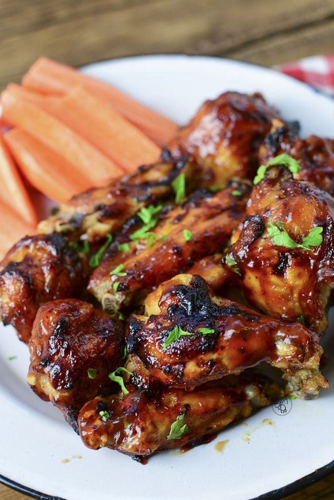 The pile of wings sitting on a white tin plate with carrot sticks in the background.