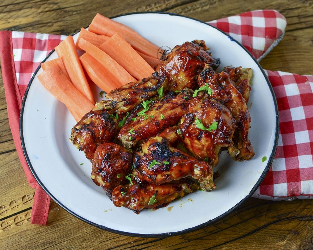 The chicken wings sitting on a red checked grilling oven mitt on a wood background.