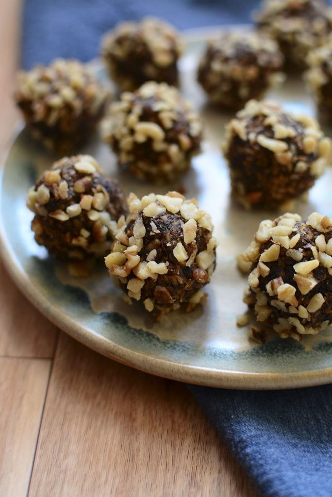 About 8 date balls arranged on a blue and grey pottery plate with a blue napkin underneath.