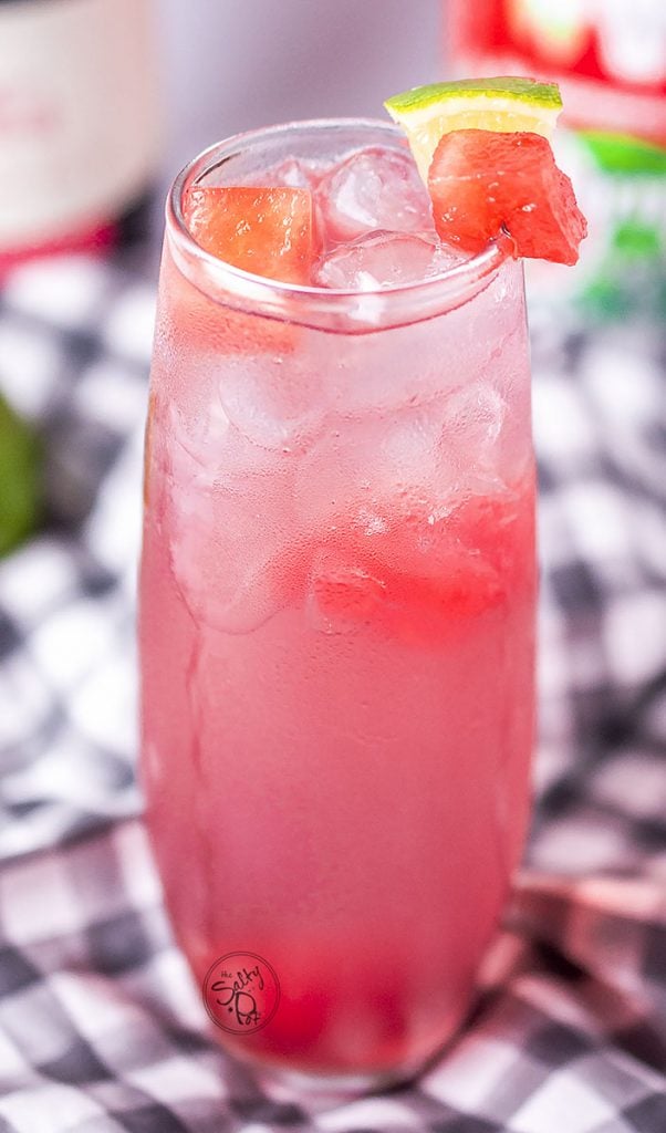 Watermelon vodka punch in a tall frosty glass with watermelon chunks and lime around the rim. 
