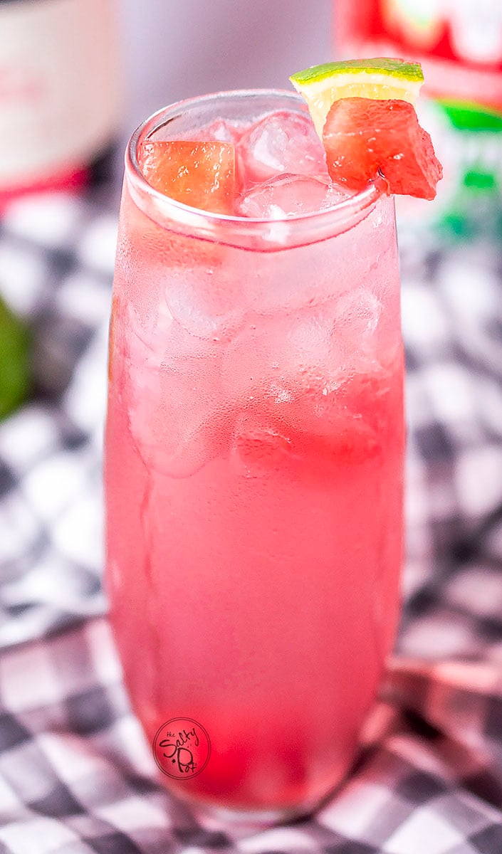 Watermelon vodka punch in a tall frosty glass with watermelon chunks and lime around the rim. 