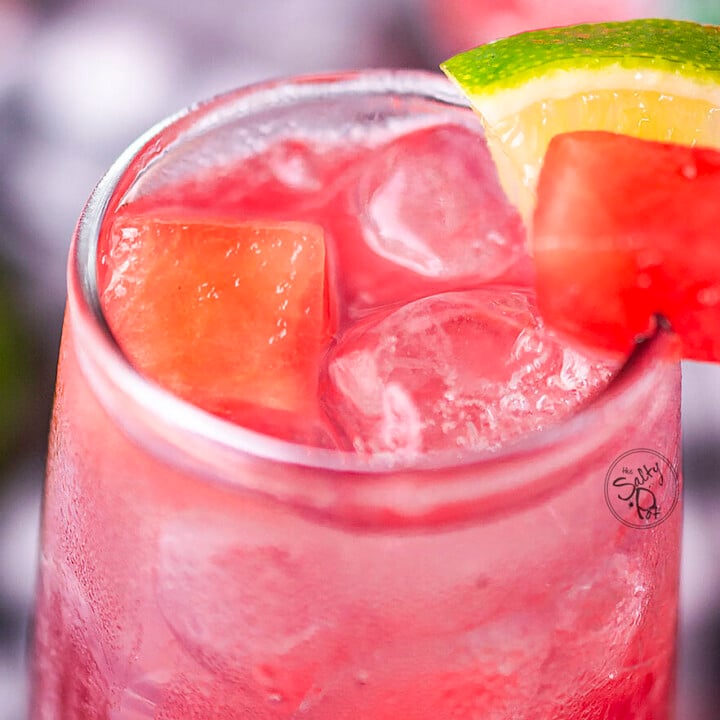 Watermelon Vodka punch in a glass with ice. There are cubes of watermelon and lime on the glass.