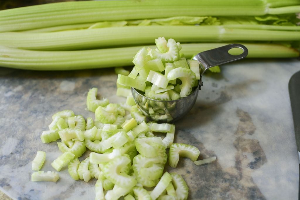 A celery bunch is in the background with cut celery sitting in front of it. 
