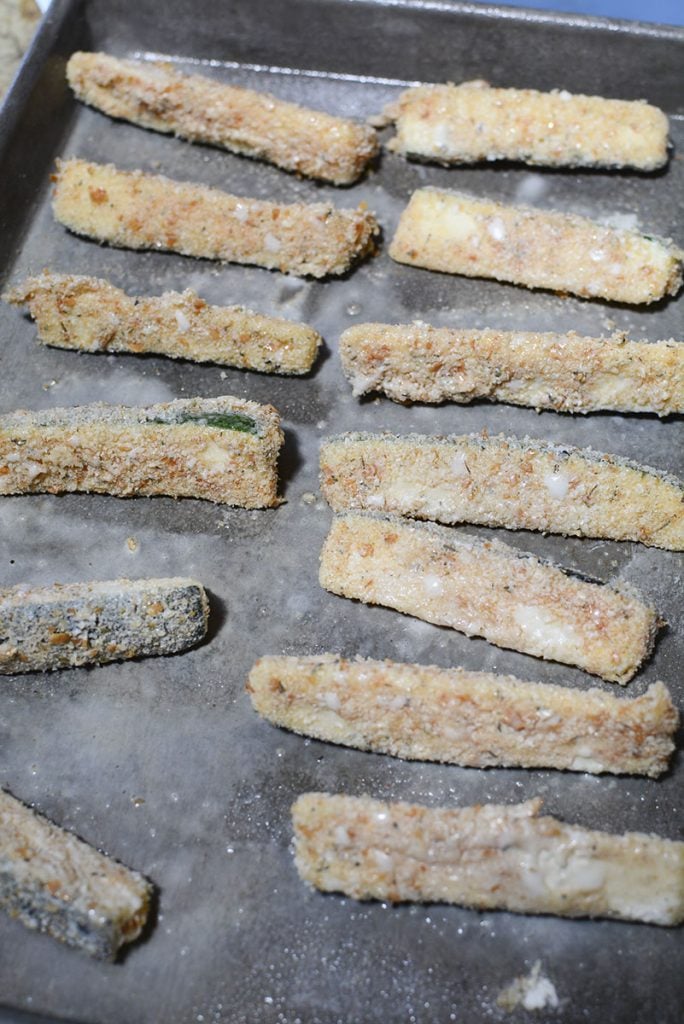 Coated Zucchini fries sitting on a pan that has been sprayed with cooking oil, ready for air frying.