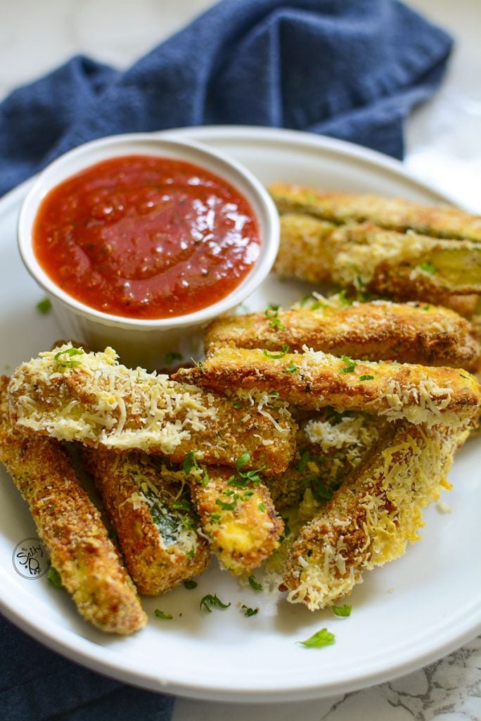 A closeup photo of the air fryer zucchini with marinara sauce on the side.