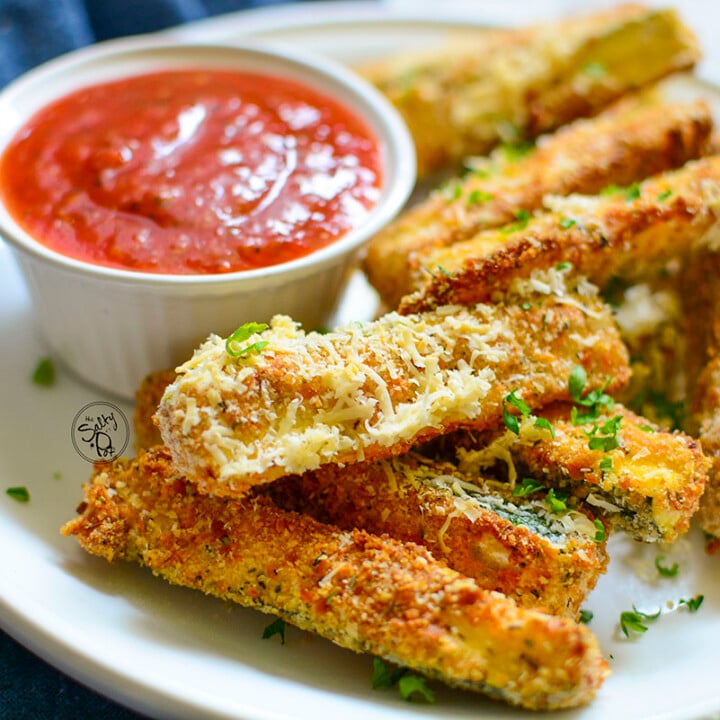 Zucchini sticks on a white plate with marinara sauce in the background.