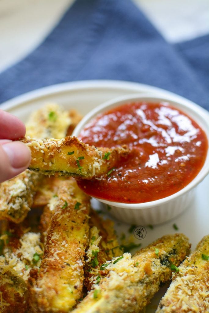 A zucchini stick that's been dipped into a bowl of marinara sauce.
