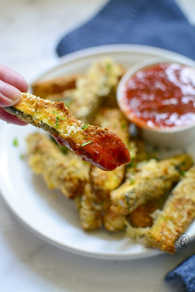 A zucchini stick with marinara on it.